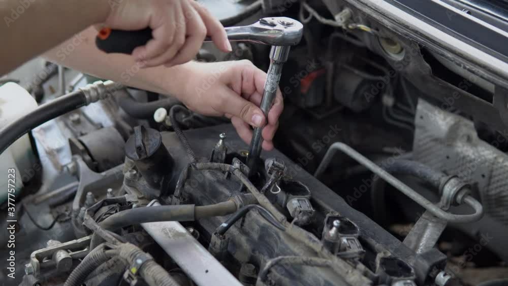 A man unscrews an old spark plug from a car engine with a tool A man unscrews an old spark plug from a car engine with a tool