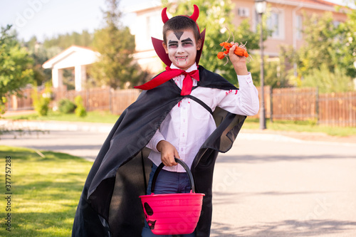Smiling boy in halloween costume of devil with horns on his head holding treats photo