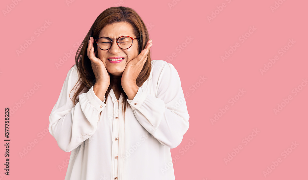 Middle age latin woman wearing casual clothes and glasses covering ears with fingers with annoyed expression for the noise of loud music. deaf concept. Middle age latin woman wearing casual clothes and glasses covering ears with fingers with annoyed expression for the noise of loud music. deaf concept.