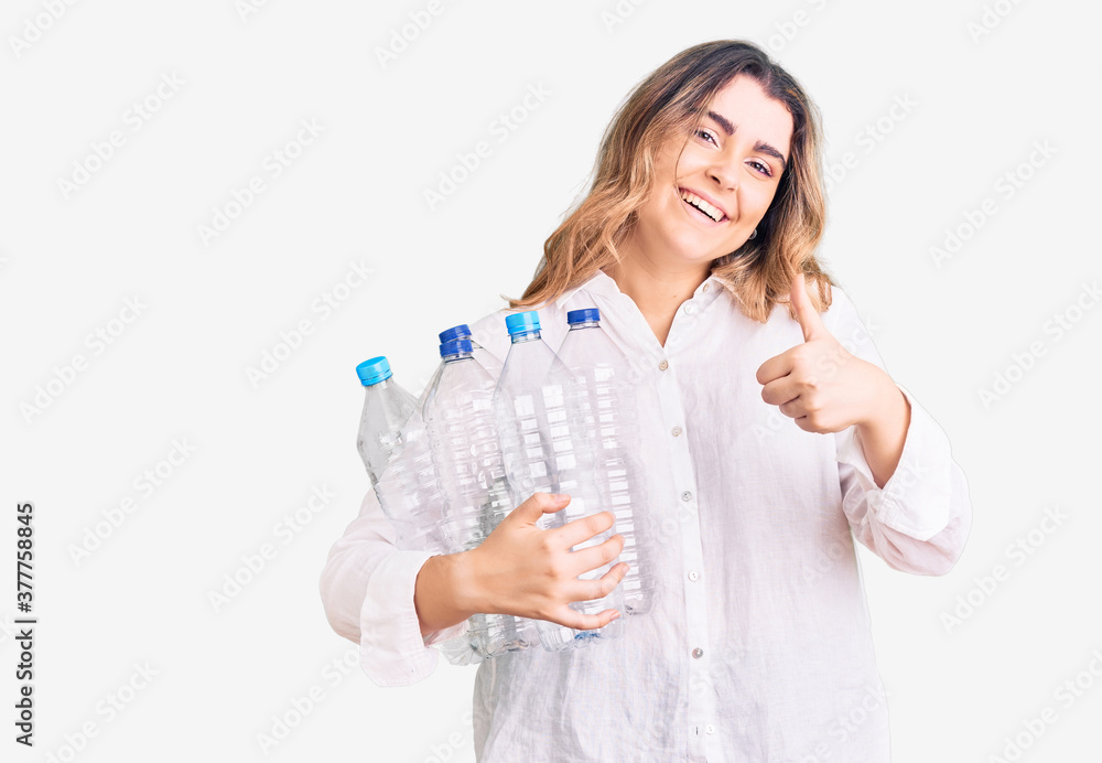 Young caucasian woman holding recycling plastic bottles smiling happy and positive, thumb up doing excellent and approval sign Young caucasian woman holding recycling plastic bottles smiling happy and positive, thumb up doing excellent and approval sign
