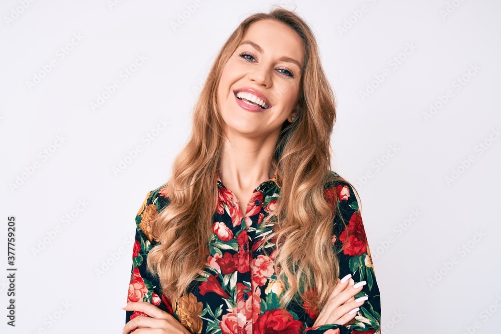 Young caucasian woman with blond hair wearing elegant floral shirt happy face smiling with crossed arms looking at the camera. positive person.
