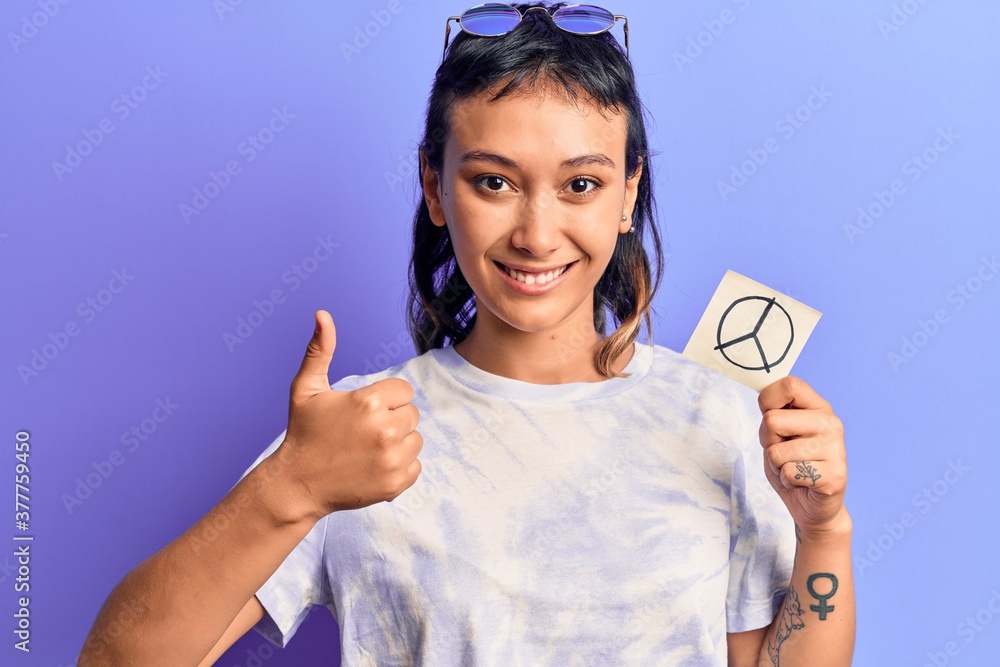 Young woman holding peace symbol reminder paper smiling happy and positive, thumb up doing excellent and approval sign Young woman holding peace symbol reminder paper smiling happy and positive, thumb up doing excellent and approval sign