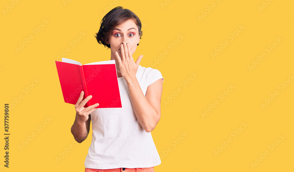 Beautiful young woman with short hair reading a book covering mouth with hand, shocked and afraid for mistake. surprised expression Beautiful young woman with short hair reading a book covering mouth with hand, shocked and afraid for mistake. surprised expression