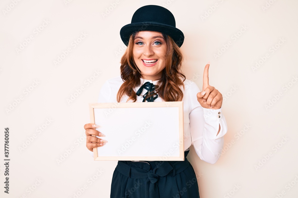 Young beautiful caucasian woman holding banner with blank space smiling with an idea or question pointing finger with happy face, number one Young beautiful caucasian woman holding banner with blank space smiling with an idea or question pointing finger with happy face, number one