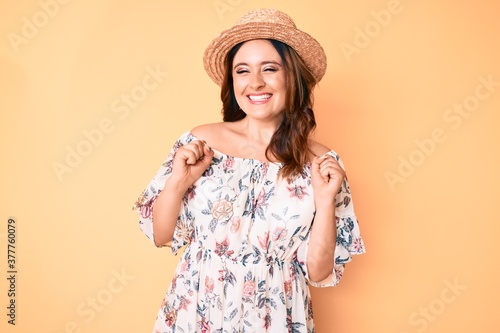 Young beautiful caucasian woman wearing summer dress and hat excited for success with arms raised and eyes closed celebrating victory smiling. winner concept.