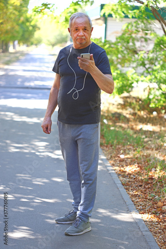 Fototapeta Naklejka Na Ścianę i Meble -  Senior man in sportswear with a smartphone on the street is engaged in fitness. Senior man in sportswear for a walk. The concept of active life in older age.