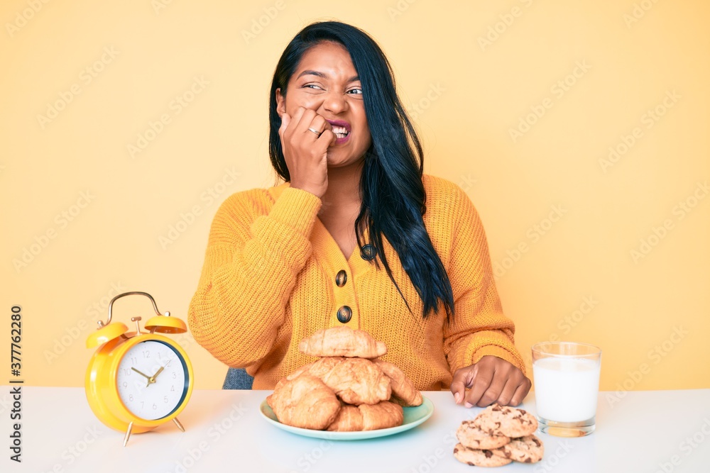 Beautiful latin young woman with long hair sitting on the table having breakfast looking stressed and nervous with hands on mouth biting nails. anxiety problem. Beautiful latin young woman with long hair sitting on the table having breakfast looking stressed and nervous with hands on mouth biting nails. anxiety problem.