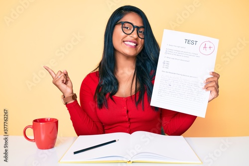 Beautiful latin young woman with long hair showing a passed exam smiling happy pointing with hand and finger to the side