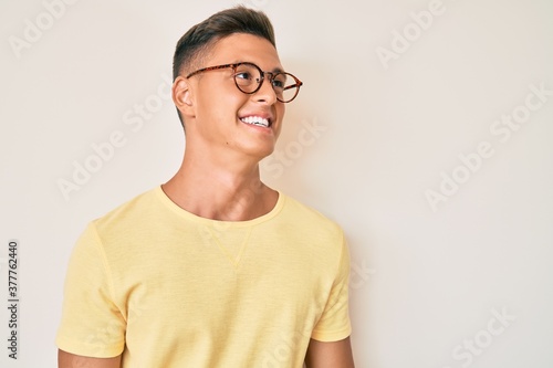 Young hispanic boy wearing casual clothes and glasses looking away to side with smile on face, natural expression. laughing confident. © Krakenimages.com