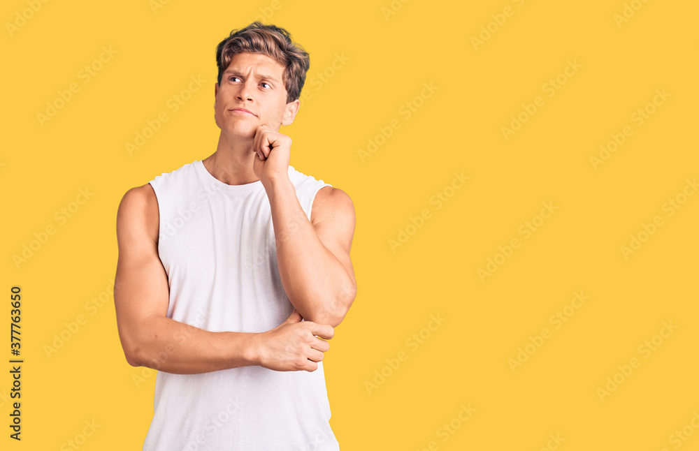 Young handsome man wearing sleveeless t shirt serious face thinking about question with hand on chin, thoughtful about confusing idea Young handsome man wearing sleveeless t shirt serious face thinking about question with hand on chin, thoughtful about confusing idea