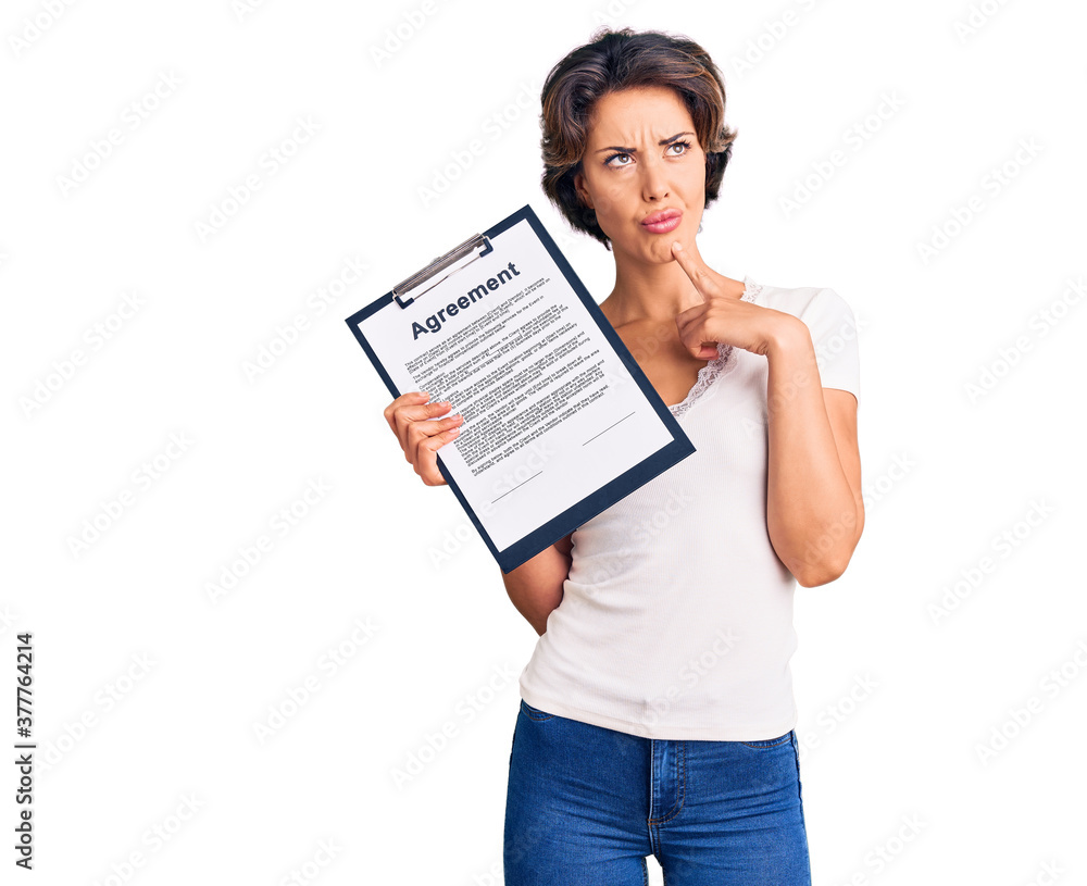 Young beautiful woman holding clipboard with agreement document serious face thinking about question with hand on chin, thoughtful about confusing idea Young beautiful woman holding clipboard with agreement document serious face thinking about question with hand on chin, thoughtful about confusing idea