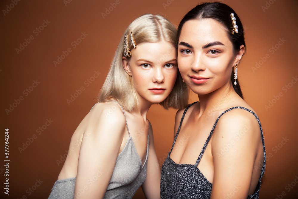 two pretty diverse girls happy posing together: blond and brunette on brown background, lifestyle people concept two pretty diverse girls happy posing together: blond and brunette on brown background, lifestyle people concept