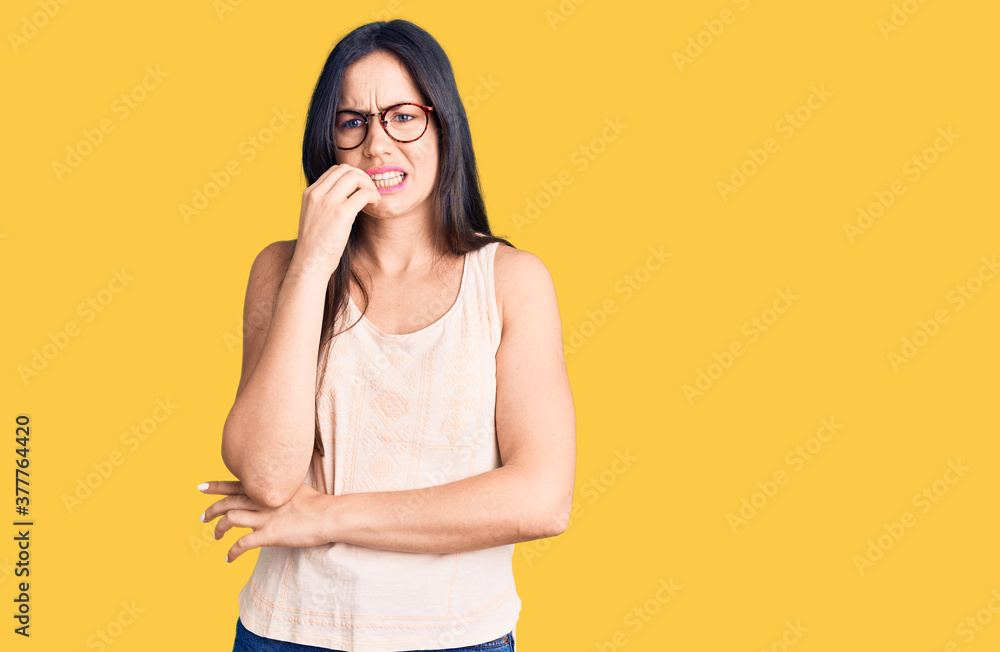 Young beautiful caucasian woman wearing casual clothes and glasses looking stressed and nervous with hands on mouth biting nails. anxiety problem. Young beautiful caucasian woman wearing casual clothes and glasses looking stressed and nervous with hands on mouth biting nails. anxiety problem.