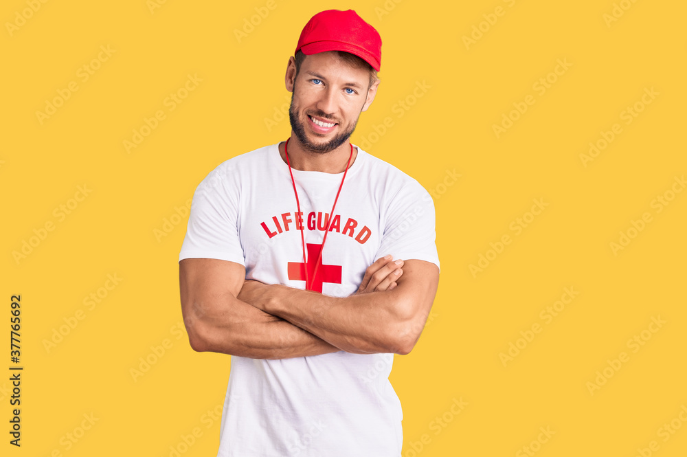 Young caucasian man wearing lifeguard t shirt holding whistle happy face smiling with crossed arms looking at the camera. positive person.