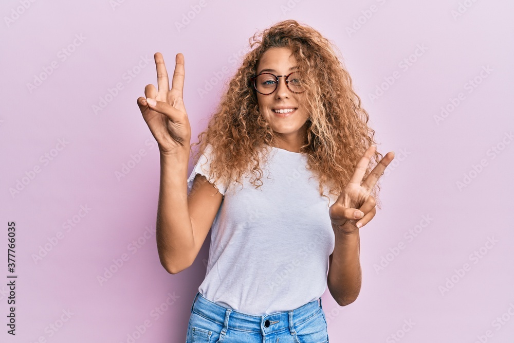 Beautiful caucasian teenager girl wearing white t-shirt over pink background smiling looking to the camera showing fingers doing victory sign. number two. Beautiful caucasian teenager girl wearing white t-shirt over pink background smiling looking to the camera showing fingers doing victory sign. number two.