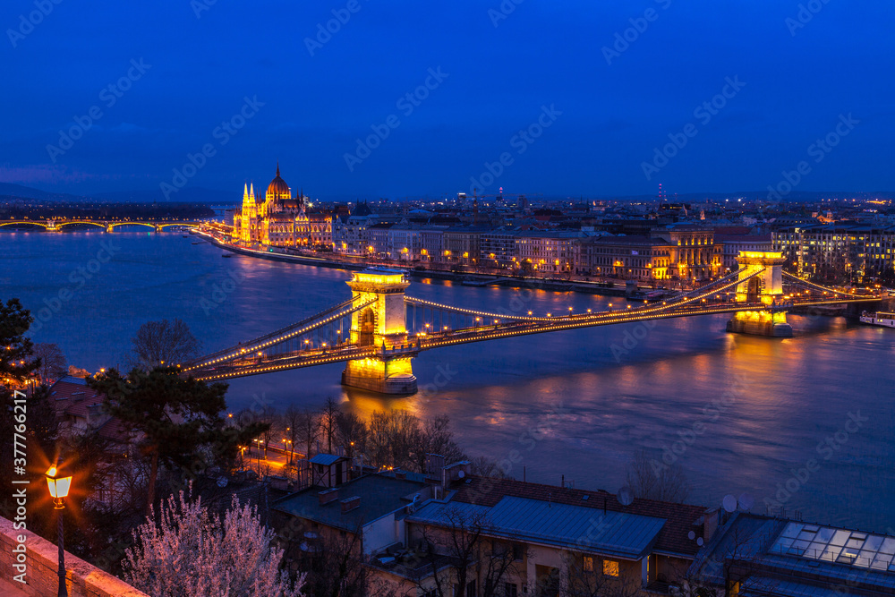 Twilight over the city of Budapest.  Seen is the Danube River and the illuminated Hungarian Parliament building and the Chain Bridge