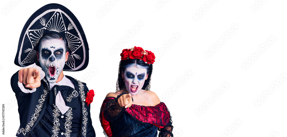 Young couple wearing mexican day of the dead costume over background pointing displeased and frustrated to the camera, angry and furious with you
