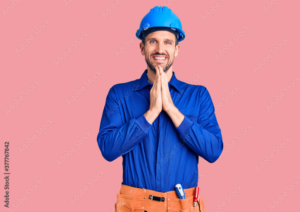 Young handsome man wearing worker uniform and hardhat praying with hands together asking for forgiveness smiling confident. Young handsome man wearing worker uniform and hardhat praying with hands together asking for forgiveness smiling confident.