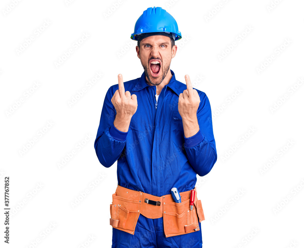 Young handsome man wearing worker uniform and hardhat showing middle finger doing fuck you bad expression, provocation and rude attitude. screaming excited Young handsome man wearing worker uniform and hardhat showing middle finger doing fuck you bad expression, provocation and rude attitude. screaming excited