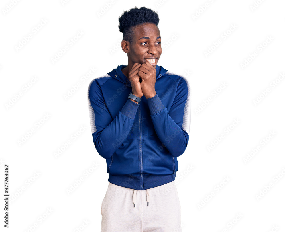 Young african american man wearing sportswear laughing nervous and excited with hands on chin looking to the side Young african american man wearing sportswear laughing nervous and excited with hands on chin looking to the side