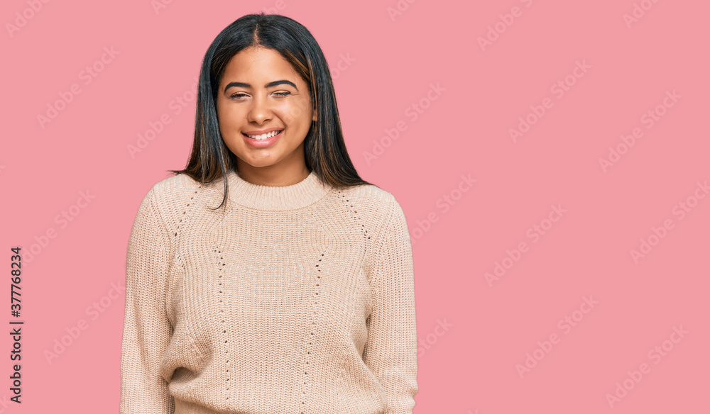 Young latin girl wearing wool winter sweater winking looking at the camera with sexy expression, cheerful and happy face. Young latin girl wearing wool winter sweater winking looking at the camera with sexy expression, cheerful and happy face.