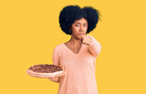 Young african american girl holding italian pizza pointing with finger to the camera and to you, confident gesture looking serious