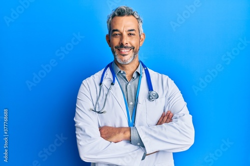 Obraz na płótnie Middle age grey-haired man wearing doctor uniform and stethoscope happy face smiling with crossed arms looking at the camera