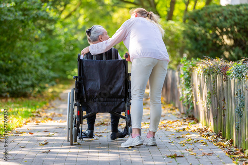 a young woman pushes an old lady in a wheelchair through a park