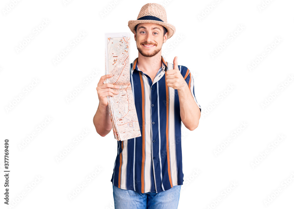 Young handsome caucasian man wearing summer hat holding city map smiling happy and positive, thumb up doing excellent and approval sign