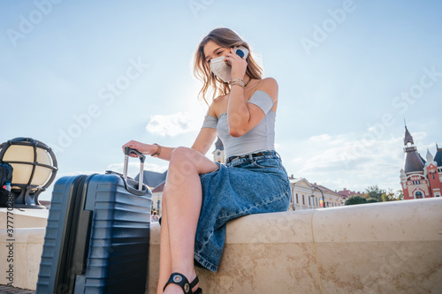 Beautiful traveler woman with a mask, with a suitcase and talking on the phone