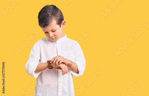 Cute blond kid wearing elegant shirt checking the time on wrist watch, relaxed and confident