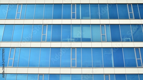 Blue curtain wall made of toned glass and steel constructions under blue sky. A fragment of a building.