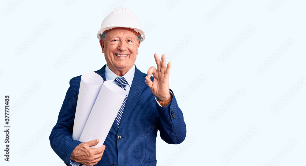 Senior handsome grey-haired man wearing architect hardhat holding blueprints doing ok sign with fingers, smiling friendly gesturing excellent symbol Senior handsome grey-haired man wearing architect hardhat holding blueprints doing ok sign with fingers, smiling friendly gesturing excellent symbol