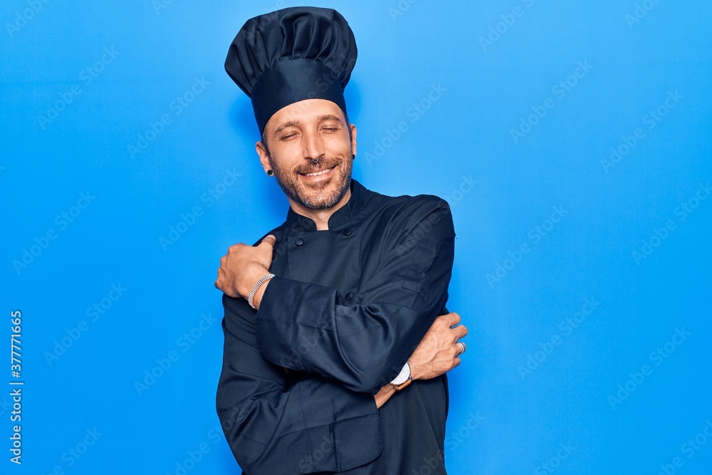 Young handsome man wearing cooker uniform hugging oneself happy and positive, smiling confident. self love and self care Young handsome man wearing cooker uniform hugging oneself happy and positive, smiling confident. self love and self care