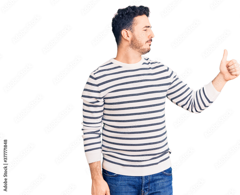Young hispanic man wearing casual clothes looking proud, smiling doing thumbs up gesture to the side Young hispanic man wearing casual clothes looking proud, smiling doing thumbs up gesture to the side