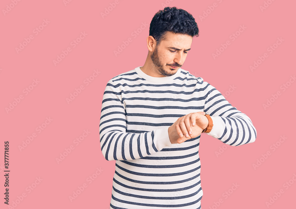 Young hispanic man wearing casual clothes checking the time on wrist watch, relaxed and confident Young hispanic man wearing casual clothes checking the time on wrist watch, relaxed and confident