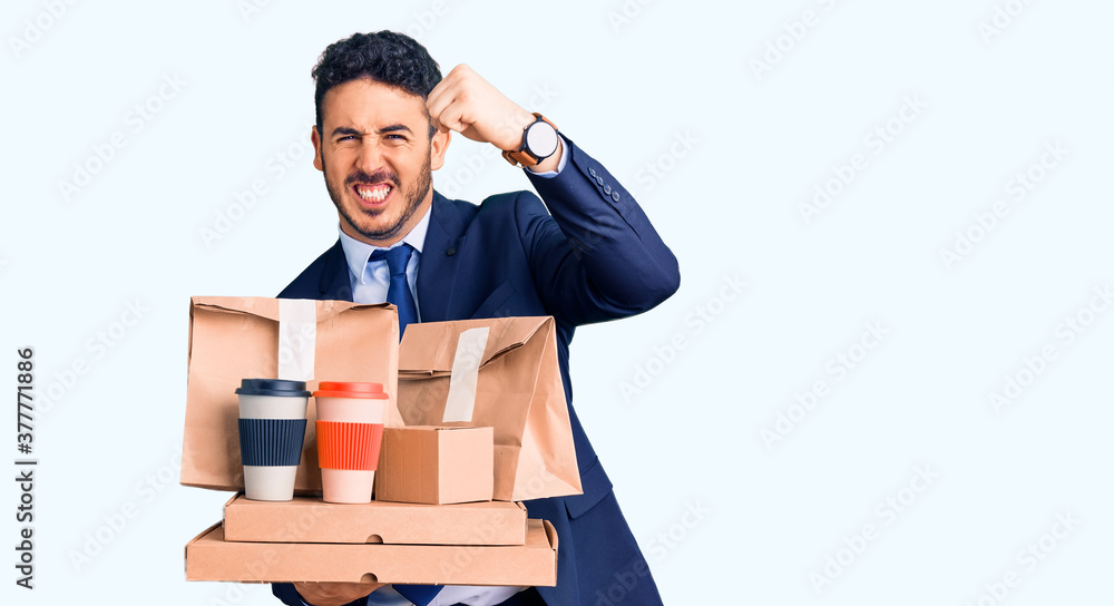 Young hispanic man wearing suit holding takeaway coffee and food annoyed and frustrated shouting with anger, yelling crazy with anger and hand raised Young hispanic man wearing suit holding takeaway coffee and food annoyed and frustrated shouting with anger, yelling crazy with anger and hand raised