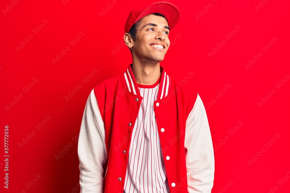 Young african amercian man wearing baseball uniform looking away to side with smile on face, natural expression. laughing confident. Young african amercian man wearing baseball uniform looking away to side with smile on face, natural expression. laughing confident.