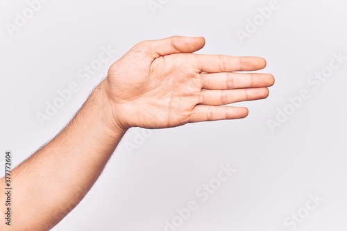 Close up of hand of young caucasian man over isolated background stretching and reaching with open hand for handshake, showing palm