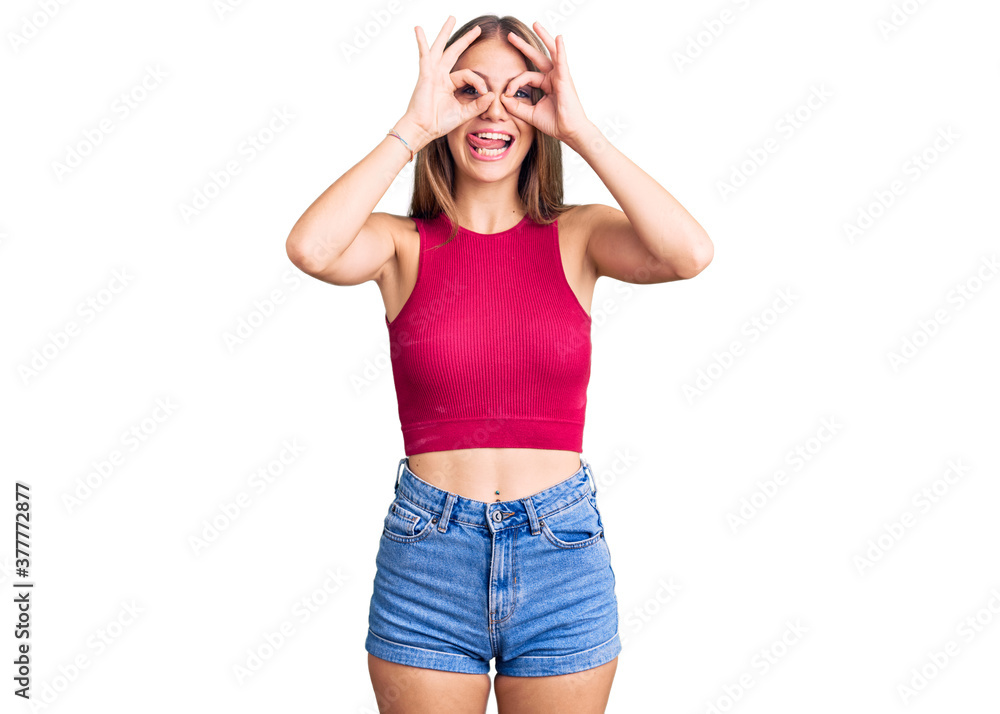 Young beautiful blonde woman wearing elegant summer shirt doing ok gesture like binoculars sticking tongue out, eyes looking through fingers. crazy expression. Young beautiful blonde woman wearing elegant summer shirt doing ok gesture like binoculars sticking tongue out, eyes looking through fingers. crazy expression.