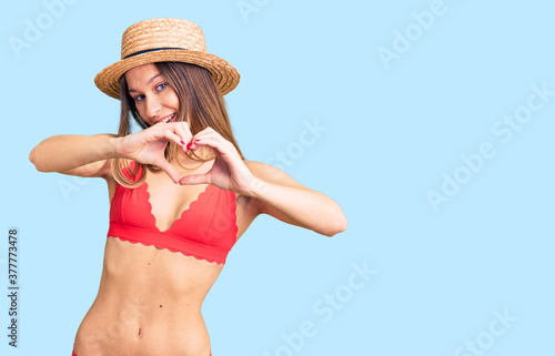 Beautiful brunette young woman wearing bikini smiling in love doing heart symbol shape with hands. romantic concept.