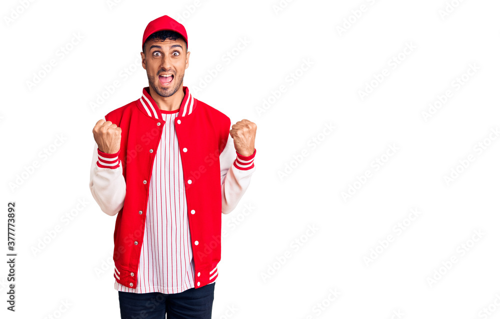 Young hispanic man wearing baseball uniform celebrating surprised and amazed for success with arms raised and open eyes. winner concept. Young hispanic man wearing baseball uniform celebrating surprised and amazed for success with arms raised and open eyes. winner concept.