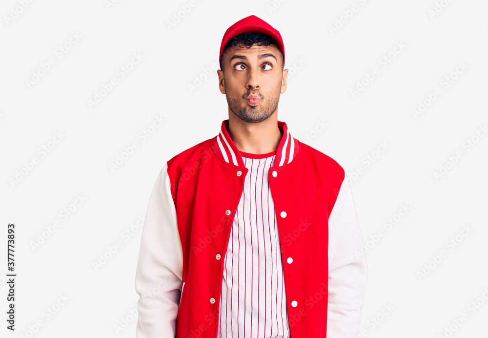 Young hispanic man wearing baseball uniform making fish face with lips, crazy and comical gesture. funny expression. Young hispanic man wearing baseball uniform making fish face with lips, crazy and comical gesture. funny expression.