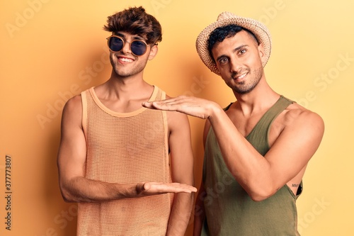 Young gay couple wearing summer clothes gesturing with hands showing big and large size sign, measure symbol. smiling looking at the camera. measuring concept.