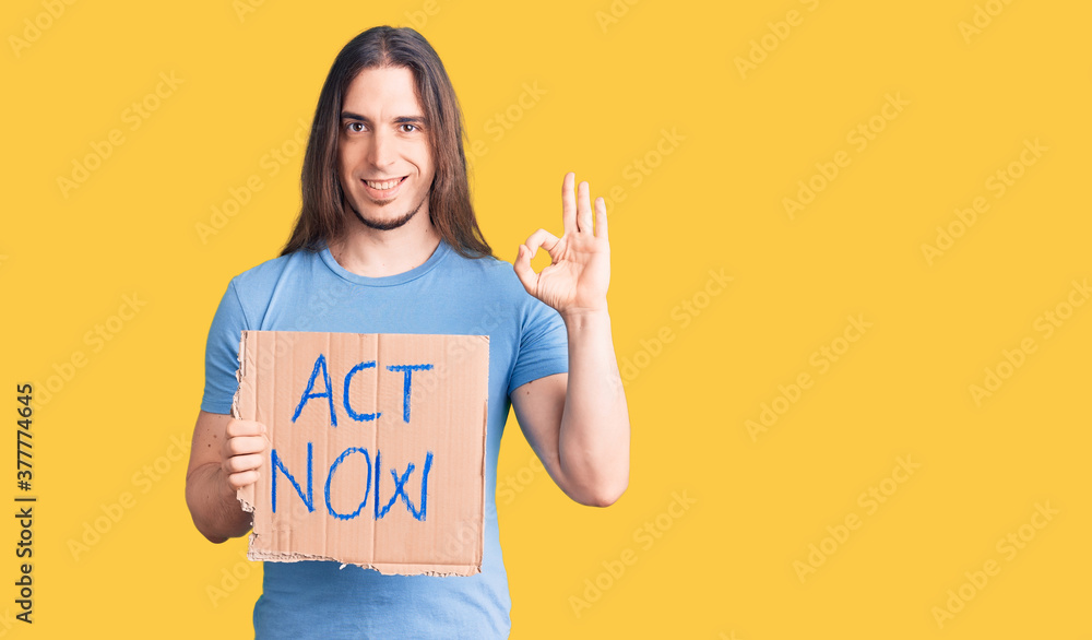 Young adult man with long hair holding act now banner doing ok sign with fingers, smiling friendly gesturing excellent symbol Young adult man with long hair holding act now banner doing ok sign with fingers, smiling friendly gesturing excellent symbol