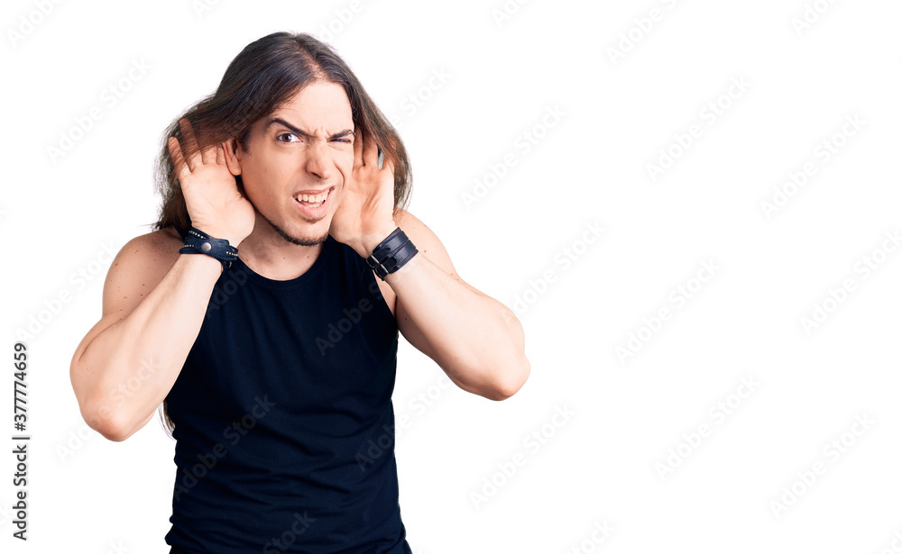 Young adult man with long hair wearing goth style with black clothes trying to hear both hands on ear gesture, curious for gossip. hearing problem, deaf Young adult man with long hair wearing goth style with black clothes trying to hear both hands on ear gesture, curious for gossip. hearing problem, deaf