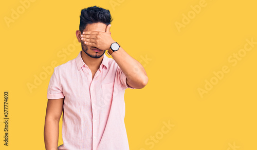 Handsome latin american young man wearing casual summer shirt covering eyes with hand, looking serious and sad. sightless, hiding and rejection concept