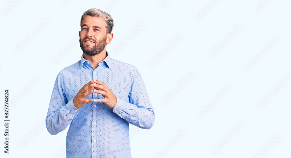 Young handsome blond man wearing elegant shirt hands together and fingers crossed smiling relaxed and cheerful. success and optimistic Young handsome blond man wearing elegant shirt hands together and fingers crossed smiling relaxed and cheerful. success and optimistic
