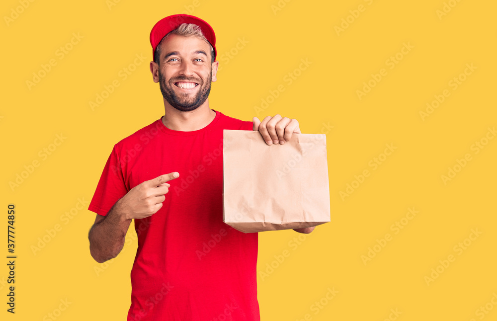 Young handsome blond man holding delivery paper bag smiling happy pointing with hand and finger Young handsome blond man holding delivery paper bag smiling happy pointing with hand and finger