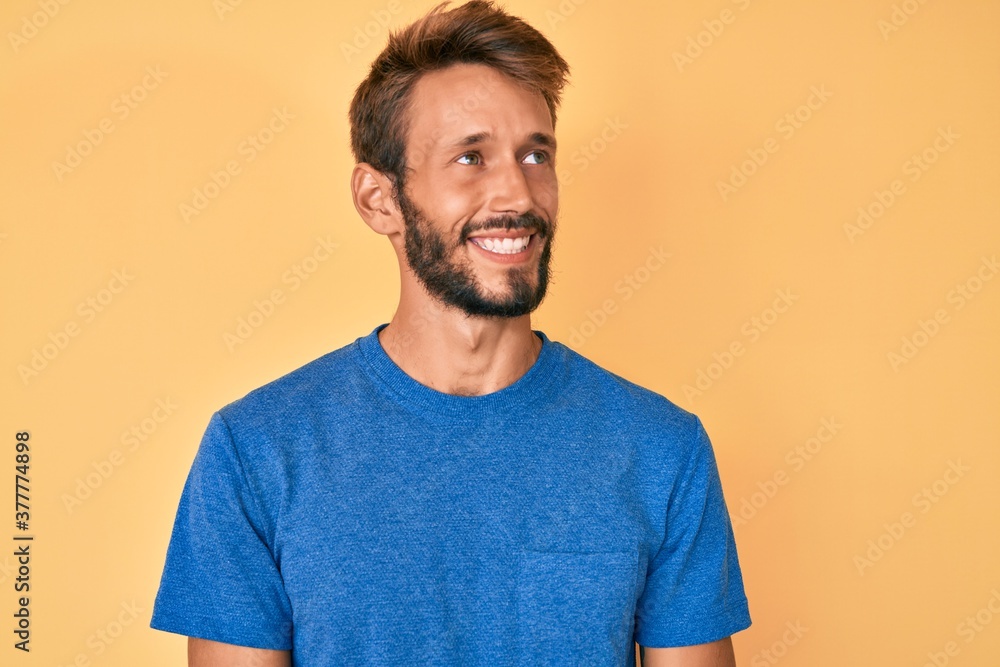 Handsome caucasian man with beard wearing casual clothes looking away to side with smile on face, natural expression. laughing confident. Handsome caucasian man with beard wearing casual clothes looking away to side with smile on face, natural expression. laughing confident.